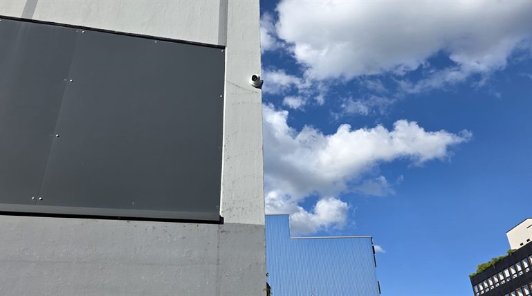 Weiße Turret-Überwachungskamera an der Ecke eines Industriegebäudes vor blauem Himmel
