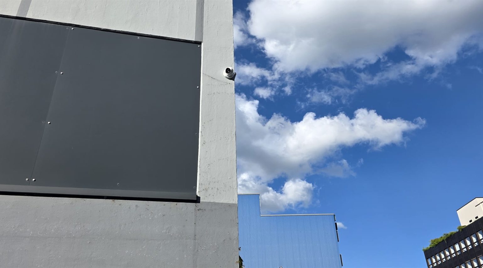 Weisse Hikvision Turret-Kamera an der Ecke eines modernen Industriegebaeudes vor blauem Himmel